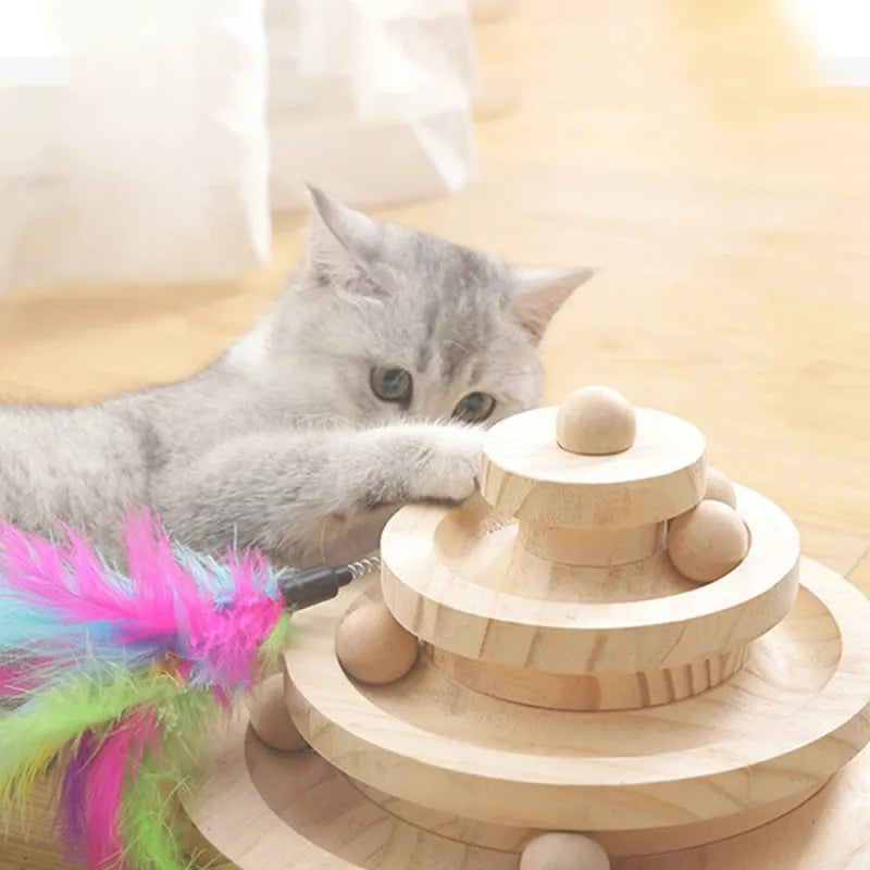 Cat playing with a wooden toy featuring colorful feathers on a light surface.
