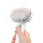 Hand holding a white grooming brush with a fluffy gray bristle head on a white background