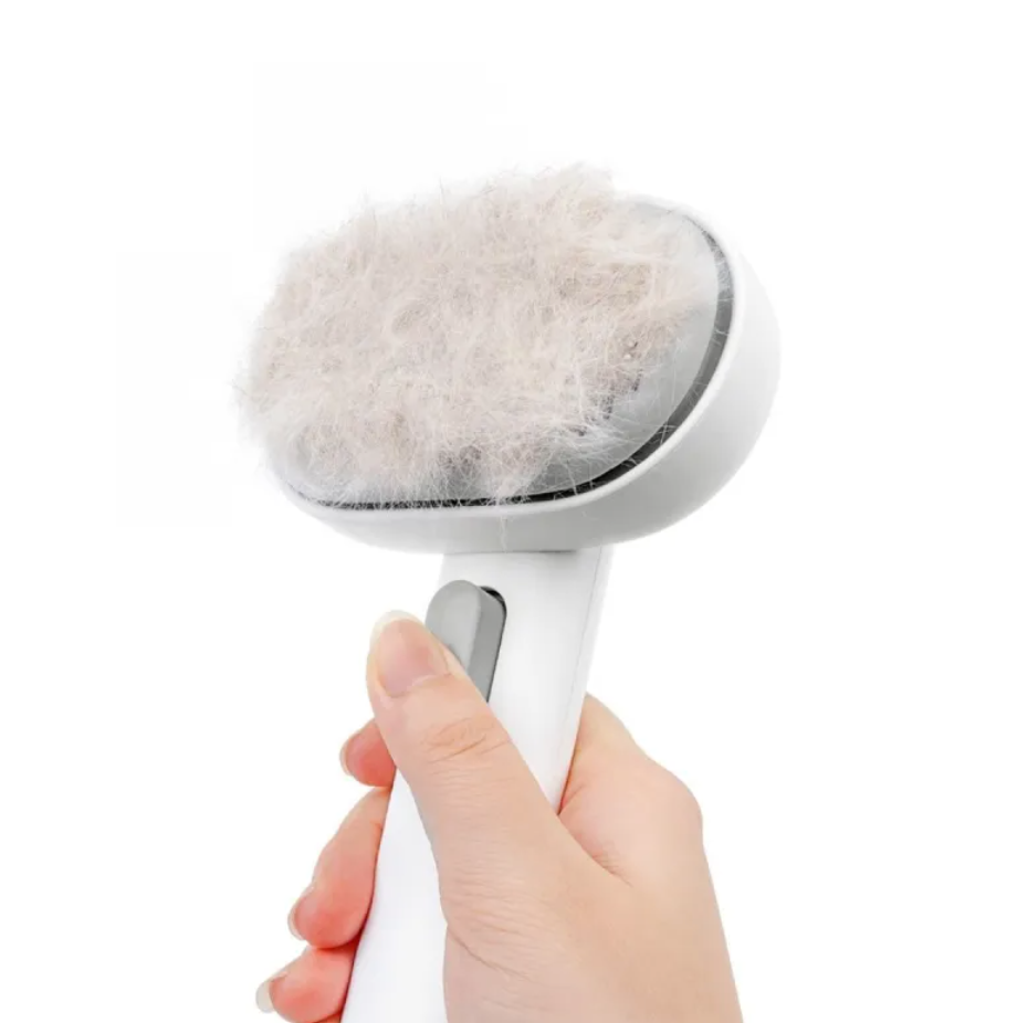 Hand holding a white grooming brush with a fluffy gray bristle head on a white background