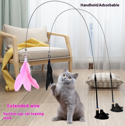 Cat playing with a feather toy on a wooden floor with a chair and cushions in the background.