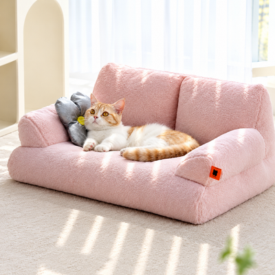 Cozy Plush Pet Sofa Bed in soft pink with an orange and white cat resting beside a gray flower pillow